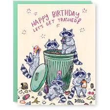 A greeting card atop a teal envelope. The front of the greeting card depicts five raccoons in various states of inebriation. The anthropomorphic raccoons are in and around a trash can, the lid of which is off and on the side of the can. Trash litters the ground. Across the top, purple text in all caps reads: 