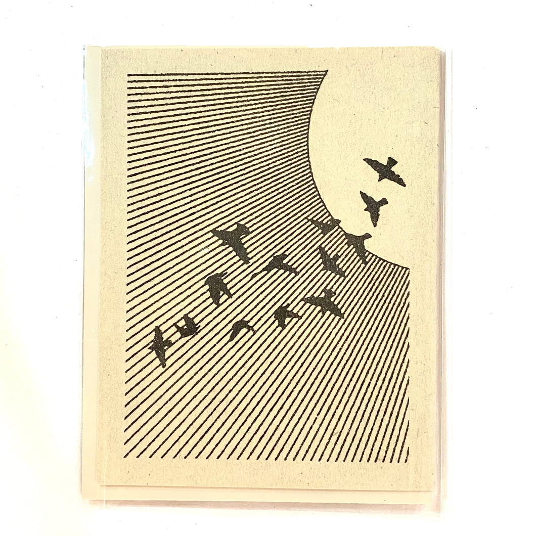 The front of a card depicts a black-and-white scene of flock of birds flying downwards diagonally away from the sun in the right hand corner. The rays of the sun beam down at the same angle as the traveling birds.
