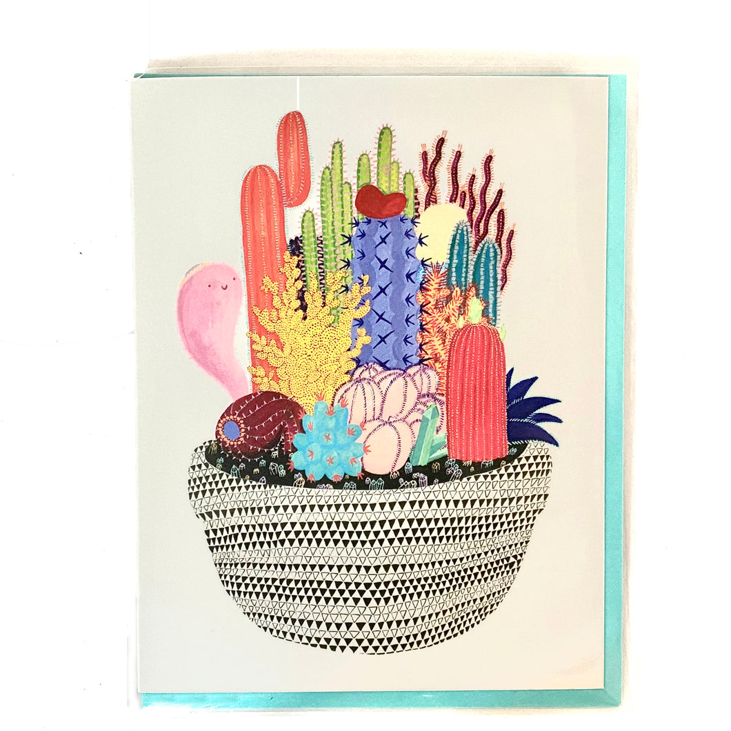 The front of this card depicts a vividly colorful garden made up of only cacti. They are in a simple black-and-white geometric patterned pot. Coming out of the pot on the left side is a smiling, pink ghost. The ghost is very cute, and not meant to be scary in any way.