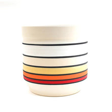 Load image into Gallery viewer, Winter Sunrise Planter: a large cylindrical planter painted with horizontal stripes. Each large stripe is a different color, with thinner black stripes in between each of the colored stripes. From top to bottom, the colors are: white, very light blush pink, light yellow, deep orange, and red.
