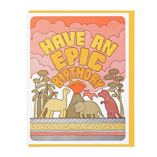 The front of this card depicts three different dinosaurs: a stegosaurus, a triceratops, and a T-rex. They are standing in front of an erupting volcano, as red smoke forms out of the volcano and into the sky. Across the smoke, stone-like text reads: 