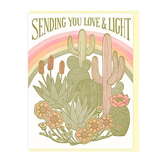 The front of this card depicts an assortment of cacti, agave, and flowers. Behind them is a rainbow. Text following the arch of the rainbow reads: 