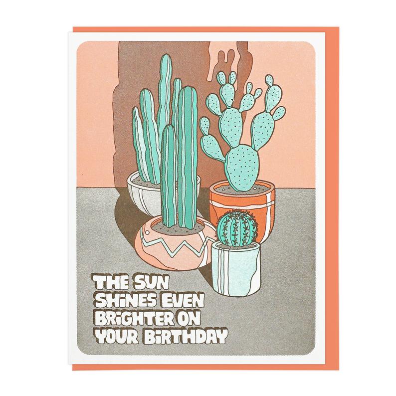 The card depicts four potted cacti of different shapes and sizes. There is a large shadow cast on the wall behind the cacti, as if the sun is shining directly on them from the front. Text in the bottom left reads: 