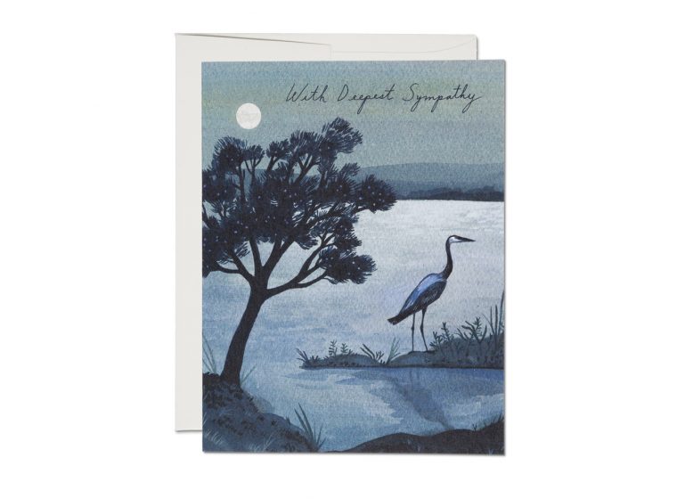 The front of the greeting card depicts a nighttime lakeside scene, with a the black silhouette of a tree on the left, leaning toward the center of the card. To the right of the tree is a heron looking off to the right. In the back we can make out some hills, as well as a bright full moon in the sky. To the right of the moon; thin, spidery script reads: 
