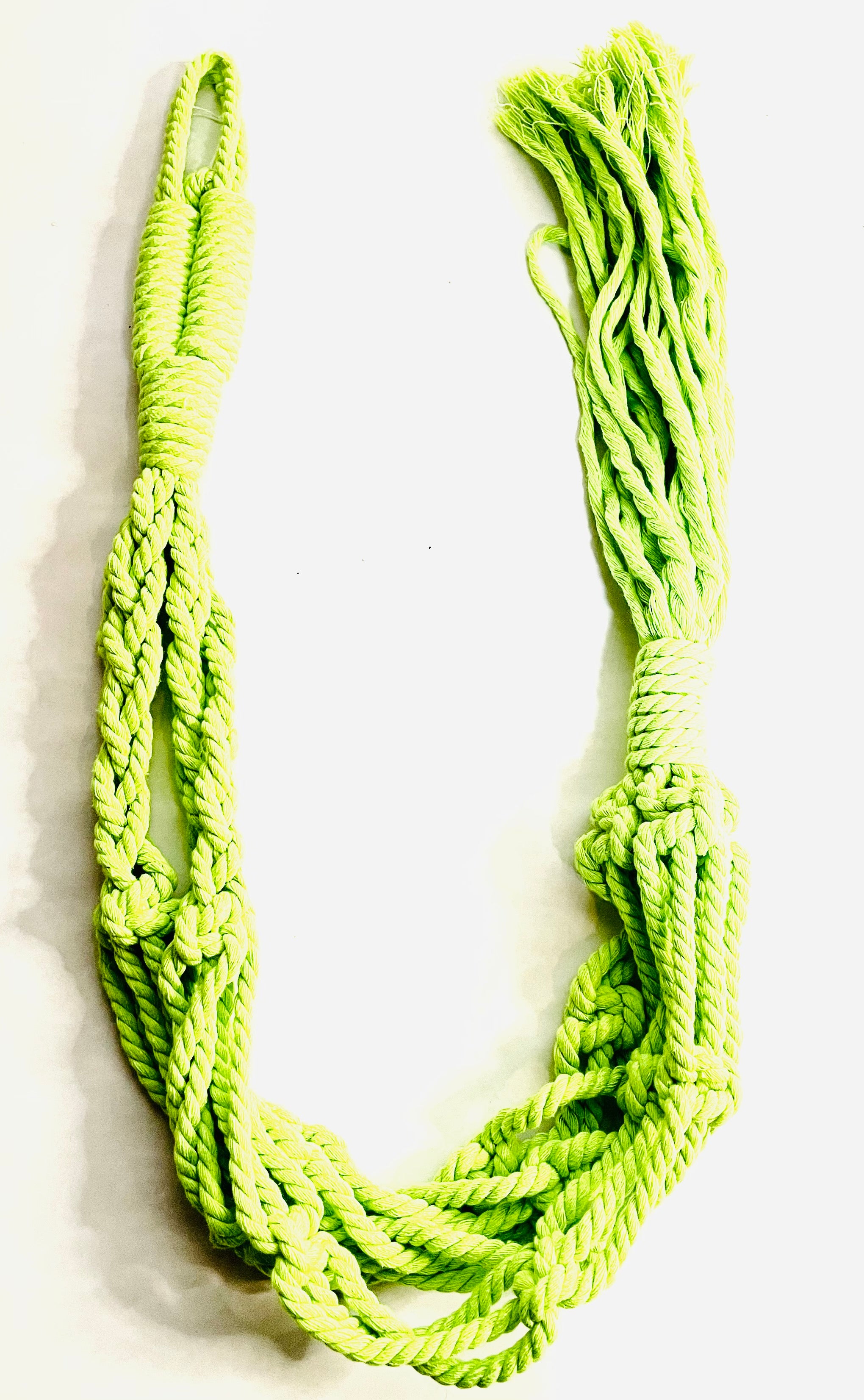 A macrame hanger lies in a U-shaped formation. The hanger is a bright highlighter green.